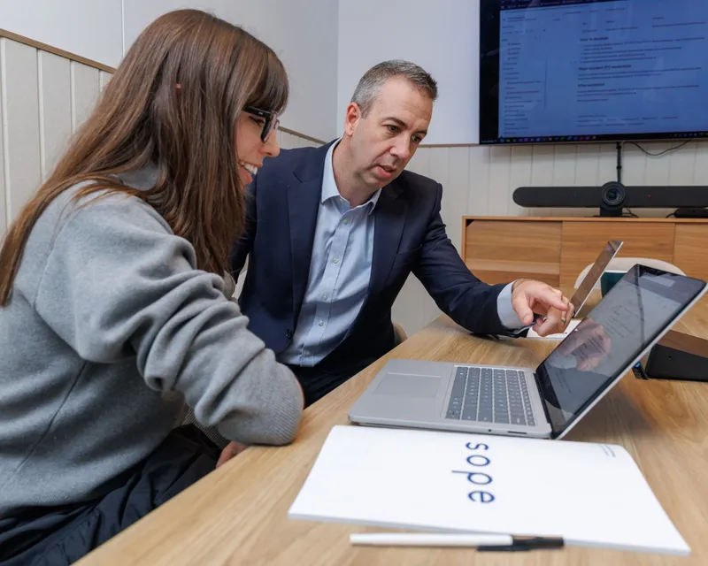 Two people at a Sope meeting table looking at a laptop together