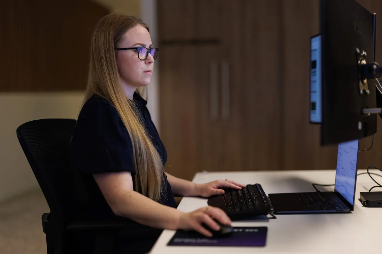 A Sope team member working at her desk with a monitor and laptop